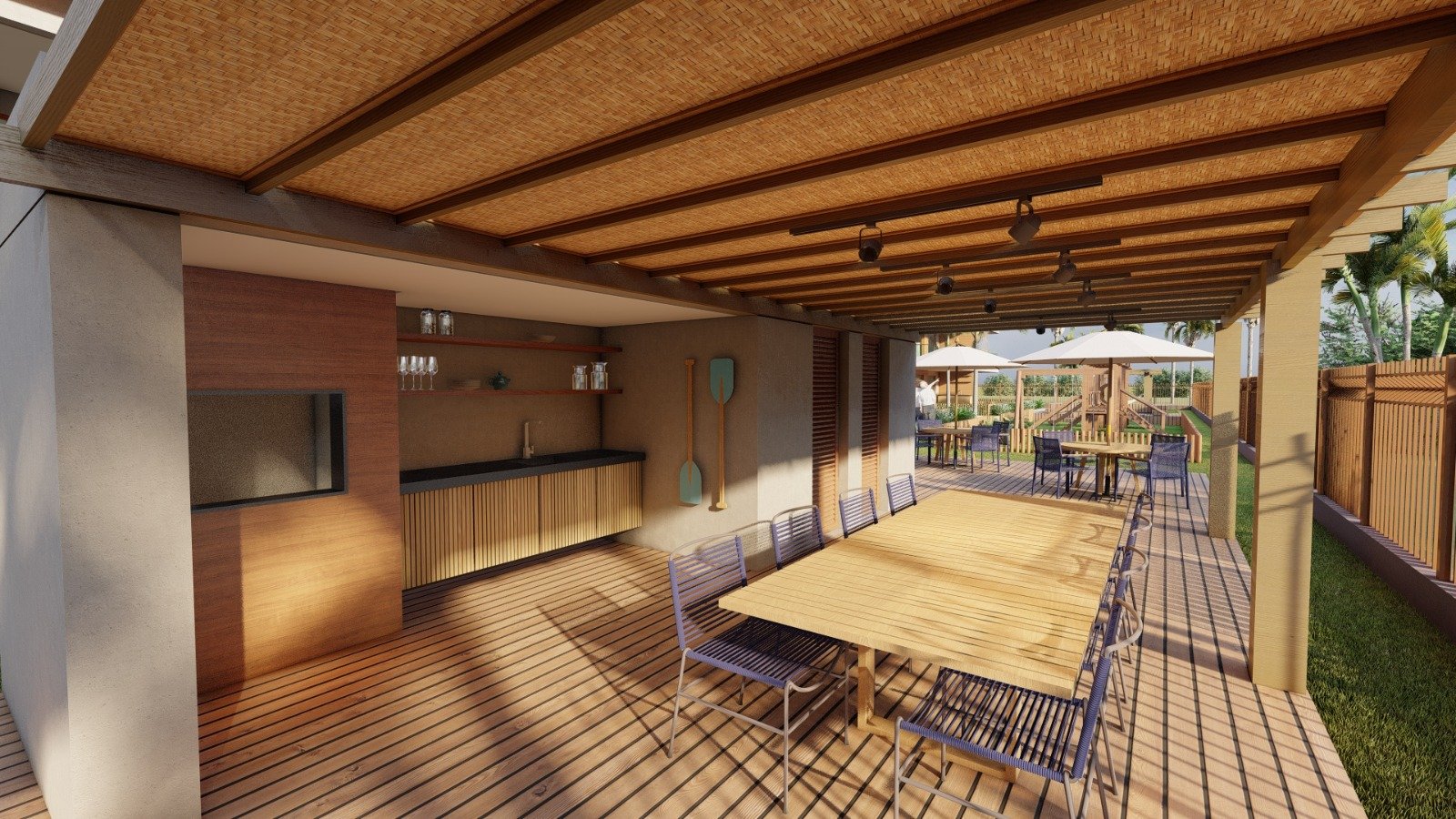 RCM Construção - Área externa com mesa de madeira grande e churrasqueira em um ambiente coberto.